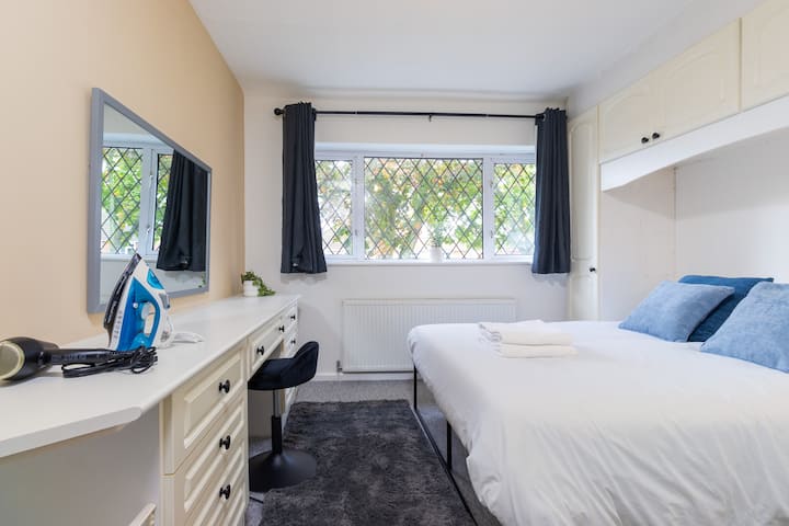 Este dormitorio bien equipado cuenta con una cama cómoda, un amplio espacio de almacenamiento, un tocador con espejo y plancha, y una ventana con luz natural.