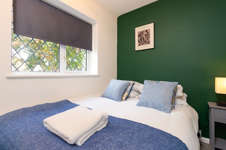 Este acogedor dormitorio cuenta con una cómoda cama doble con suaves detalles azules y una ventana con persiana de privacidad para un ambiente relajante.