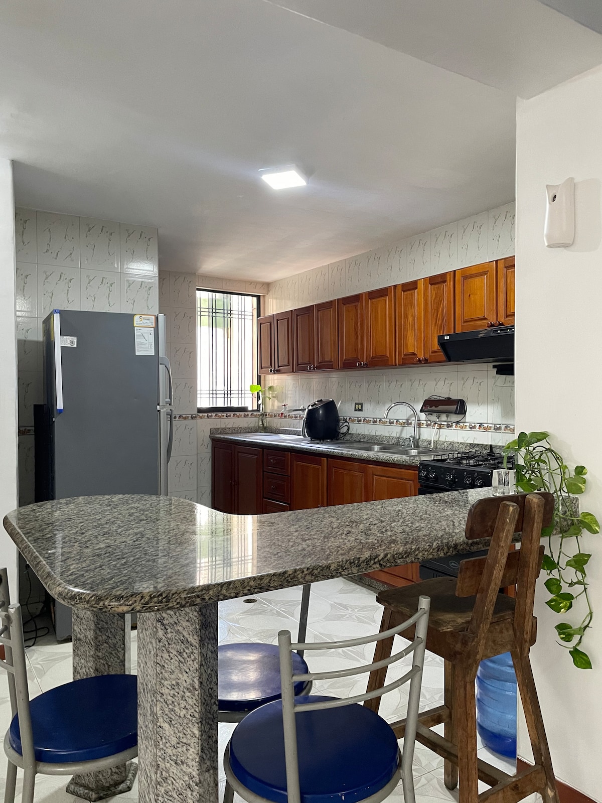 A kitchen area is shown featuring wooden cabinetry and granite countertops. A refrigerator and stove are included, along with modern faucets. A small dining table with two metal chairs is positioned near a window, providing natural light to the space.