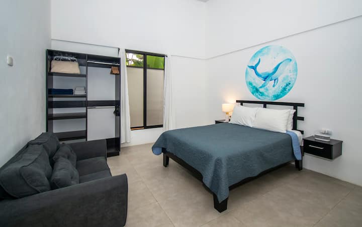 Third guest bedroom at Coral Dream House, featuring a queen-size bed, a/c, a comfy couch, a spacious closet, and views of the lush greenery surrounding the property, creating a cozy and inviting retreat.