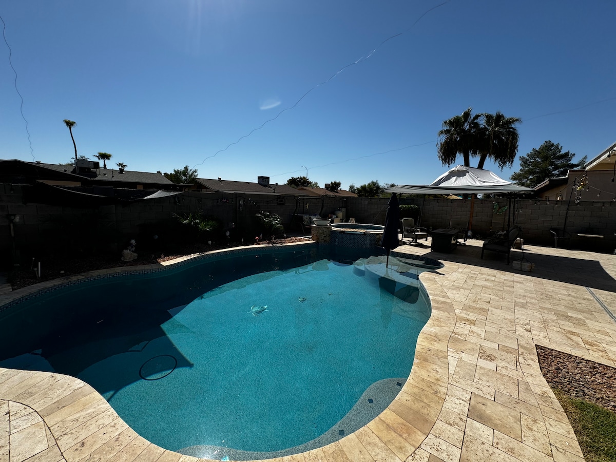 A private pool is surrounded by a spacious patio area featuring lounge chairs and a shaded sitting area. Sunlight reflects off the clear water, and palm trees are visible in the background, creating a tranquil atmosphere for relaxation.