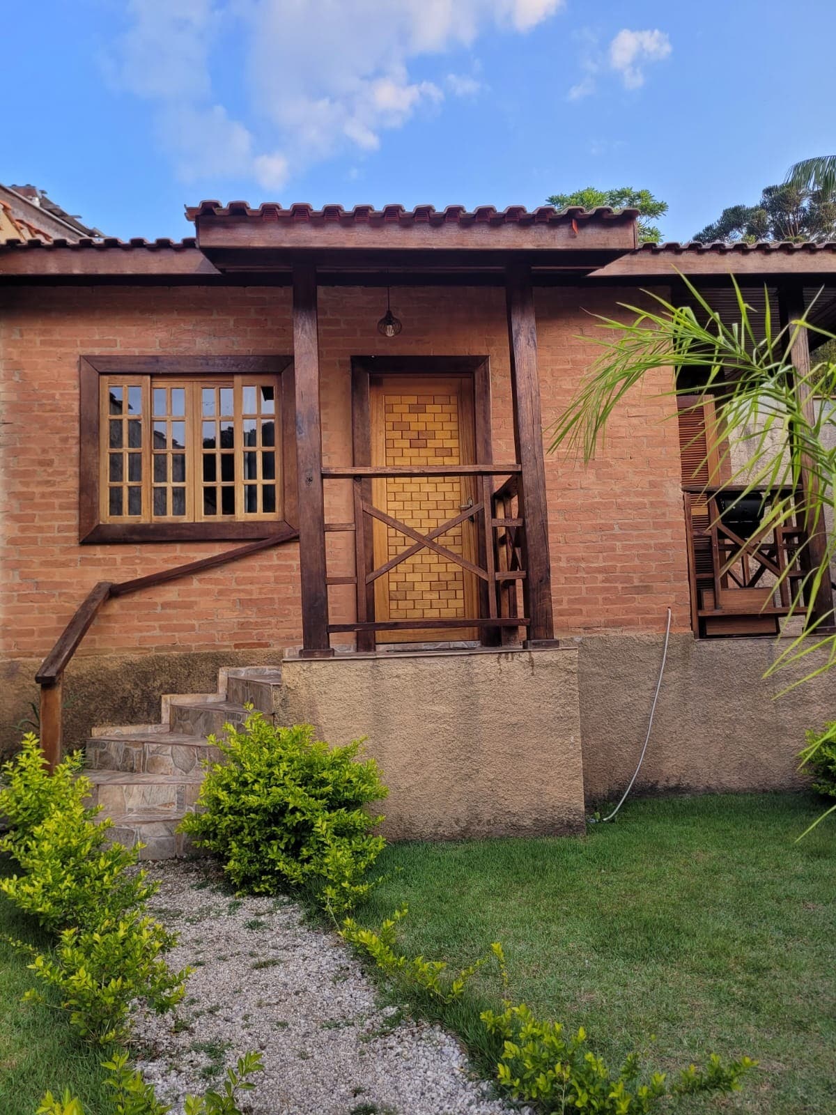 A charming entrance features wooden framing and a textured door, surrounded by brick walls. Steps lead up to the entrance, flanked by lush greenery and a well-maintained path connecting to the vibrant garden.