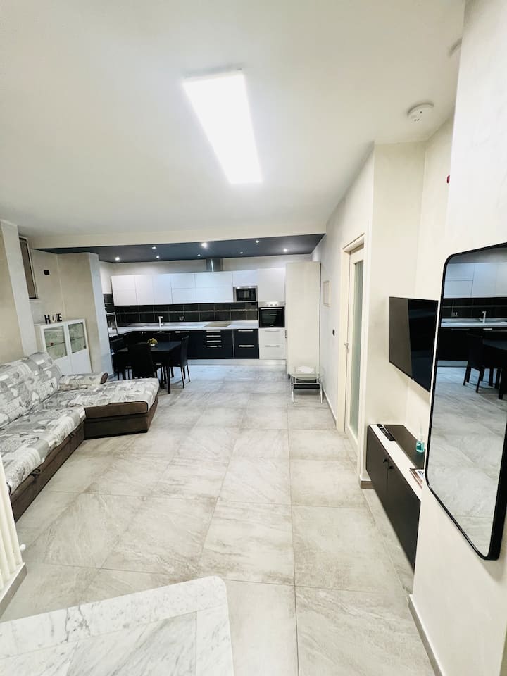 Всекидневната, сърцето на апартамента, е идеалната стая, където можете да се отпуснете заедно, благодарение на удобния диван и телевизора.