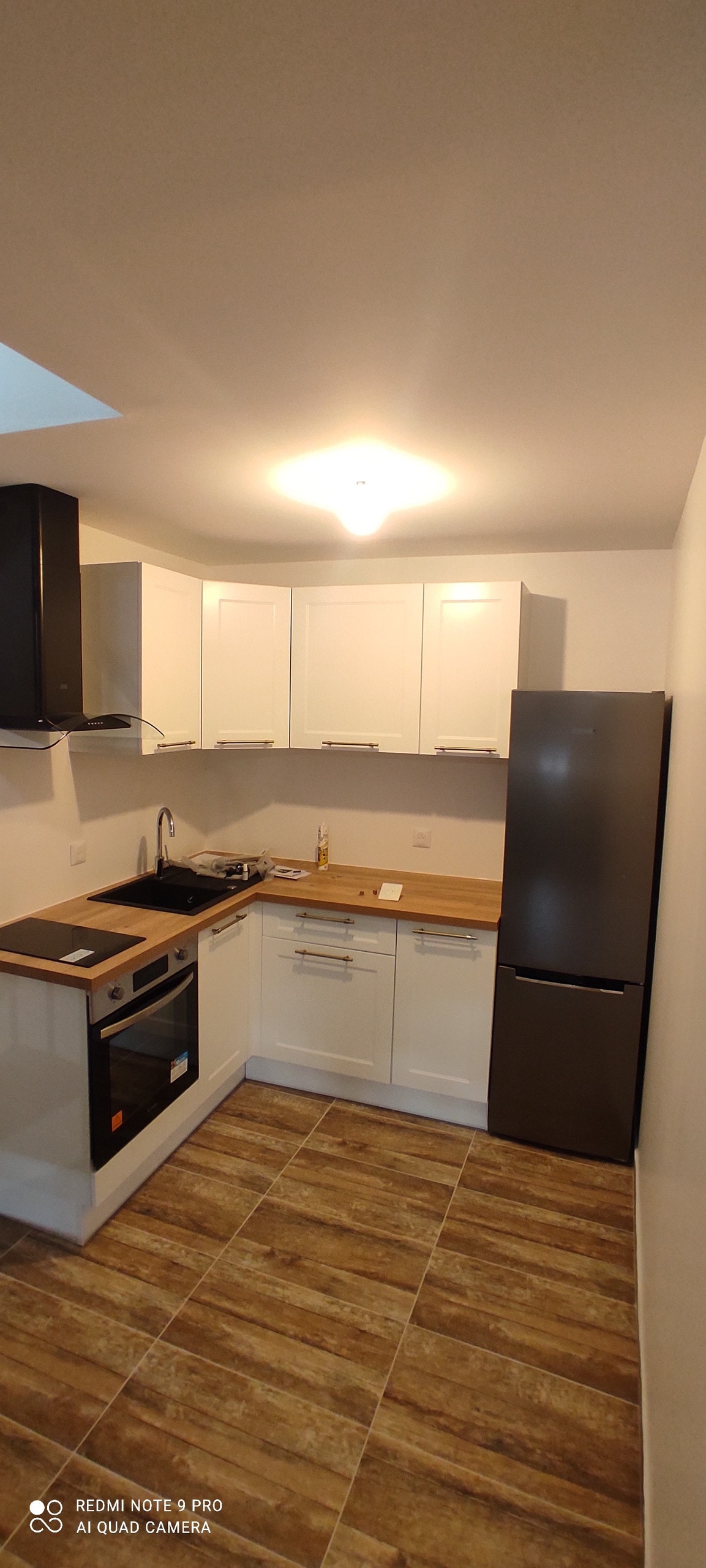 The kitchen features modern cabinetry in white and a sleek wooden countertop. Stainless steel appliances include an oven, a stovetop, and a refrigerator. Warm lighting illuminates the space, highlighting the tiled floor and efficiently organized layout.