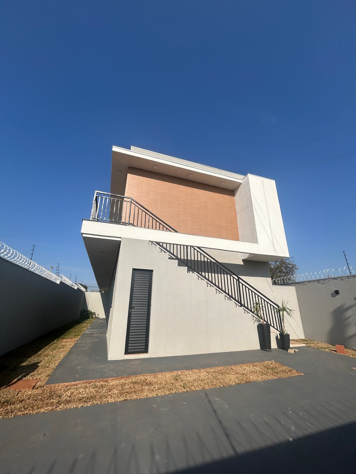 A modern two-story building showcases a clean architectural design with a striking off-white exterior and a prominent staircase leading to the upper level. Surrounded by a well-maintained path, the building is set against a clear blue sky, emphasizing its contemporary style.