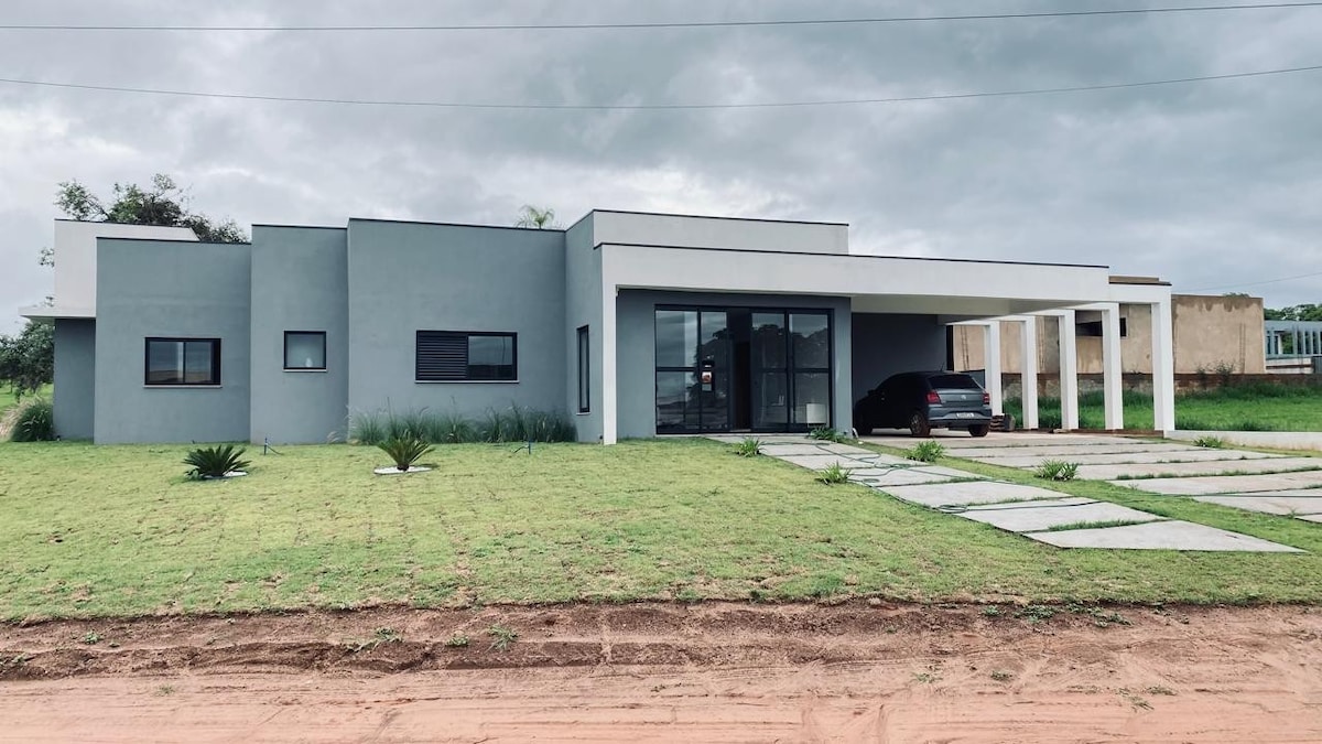 The modern exterior of the house features a clean design with large windows, a glass front door, and a wide overhang. A neatly landscaped yard with green grass and stepping stones leads to the driveway, accommodating one vehicle.