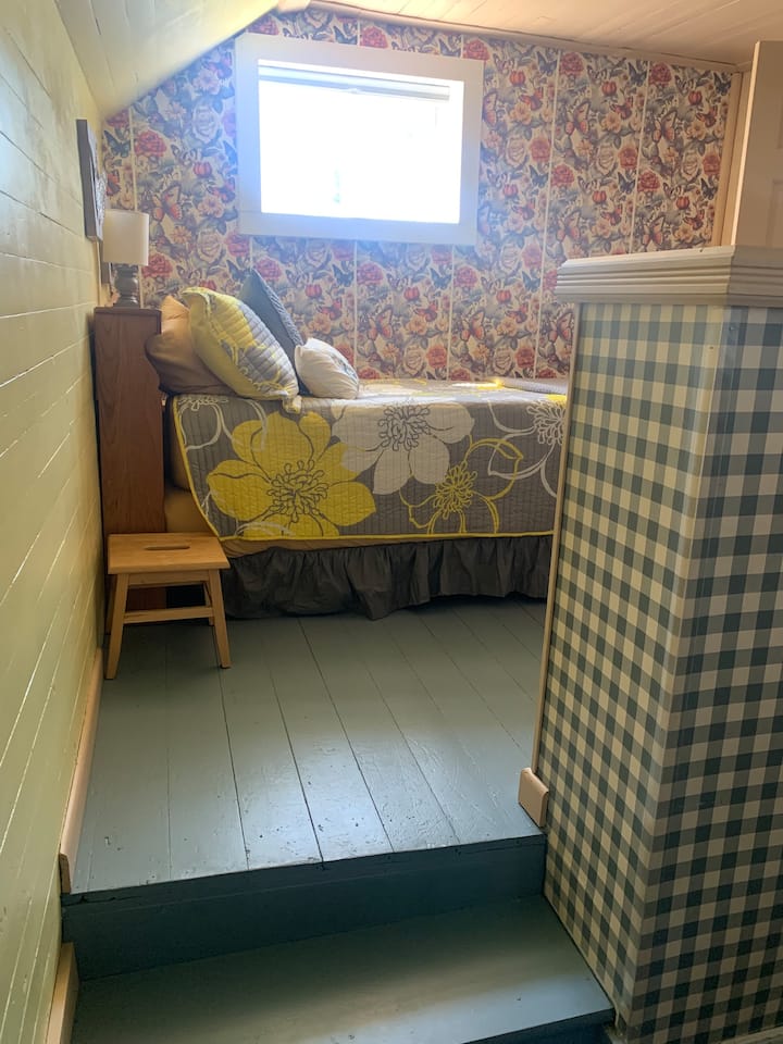 A twin bed is tucked into the open area at the top of the stairs, outside the bedrooms. While this is not a traditional bedroom (it is not fully enclosed), it does provide a sleeping space separate from other rooms.