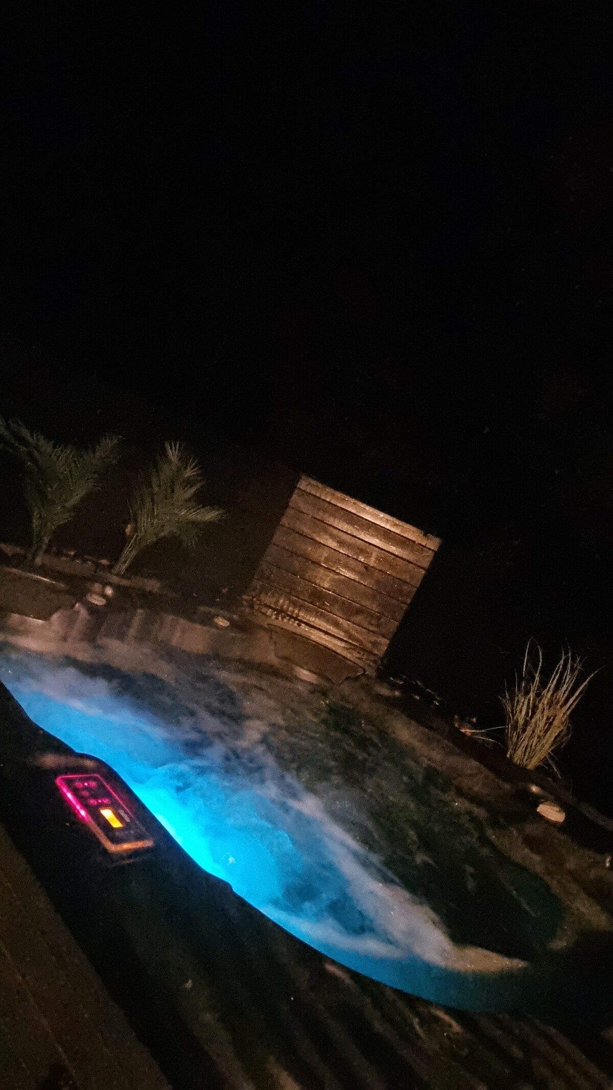 A well-maintained outdoor jacuzzi is illuminated with soothing blue lights, creating a calming atmosphere at night. Surrounding the jacuzzi are low-maintenance plants and a privacy wall, enhancing the serene ambiance for relaxation.