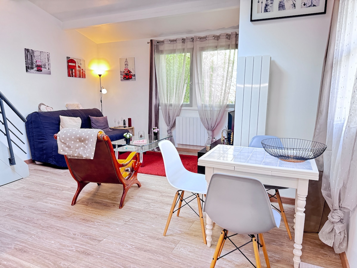 The main living area displays a blend of comfort and functionality, featuring a dark blue sofa, a vintage-style chair, and a dining table with modern chairs. Natural light enters through the window, while soft curtains add a touch of warmth to the space.