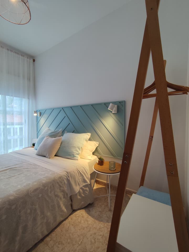 ห้องนอนคู่สบายๆ ในโทนสีฟ้าพร้อมระเบียง มีเบาะหลายใบ ผ้านวม และโคมไฟสำหรับอ่านหนังสือ 