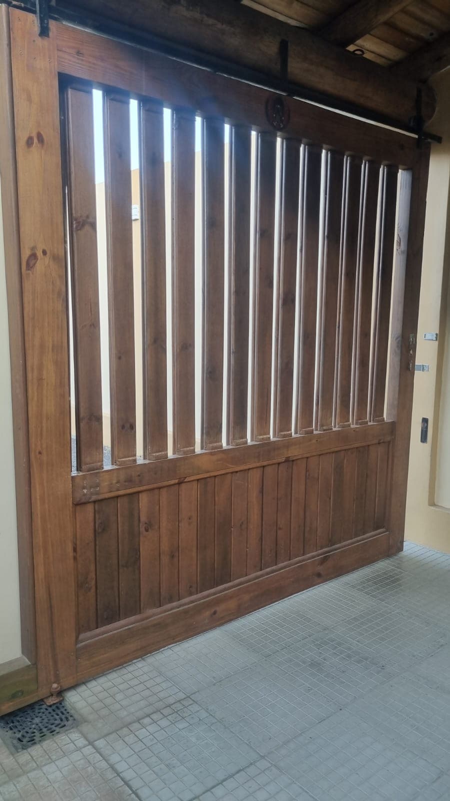 A wooden gate constructed with vertical slats allows for glimpses of light, while a solid lower panel provides privacy. The gate is framed within a wall, complementing the surrounding structures and enhancing the overall aesthetic of the entrance.