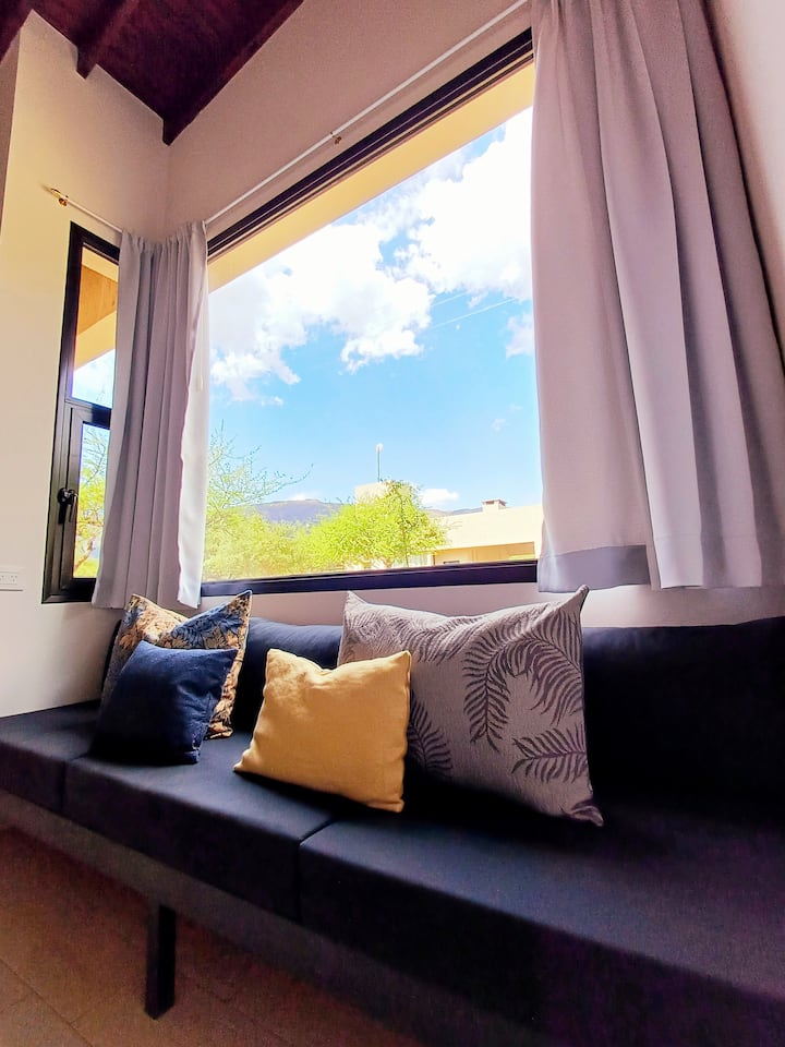 Relájate en nuestro rincón de serenidad: un cómodo sofá empotrado en una encantadora ventana con un amplio ventanal. Disfruta de la cálida luz natural mientras te sumerges en un buen libro, contemplas el paisaje o miras la TV.