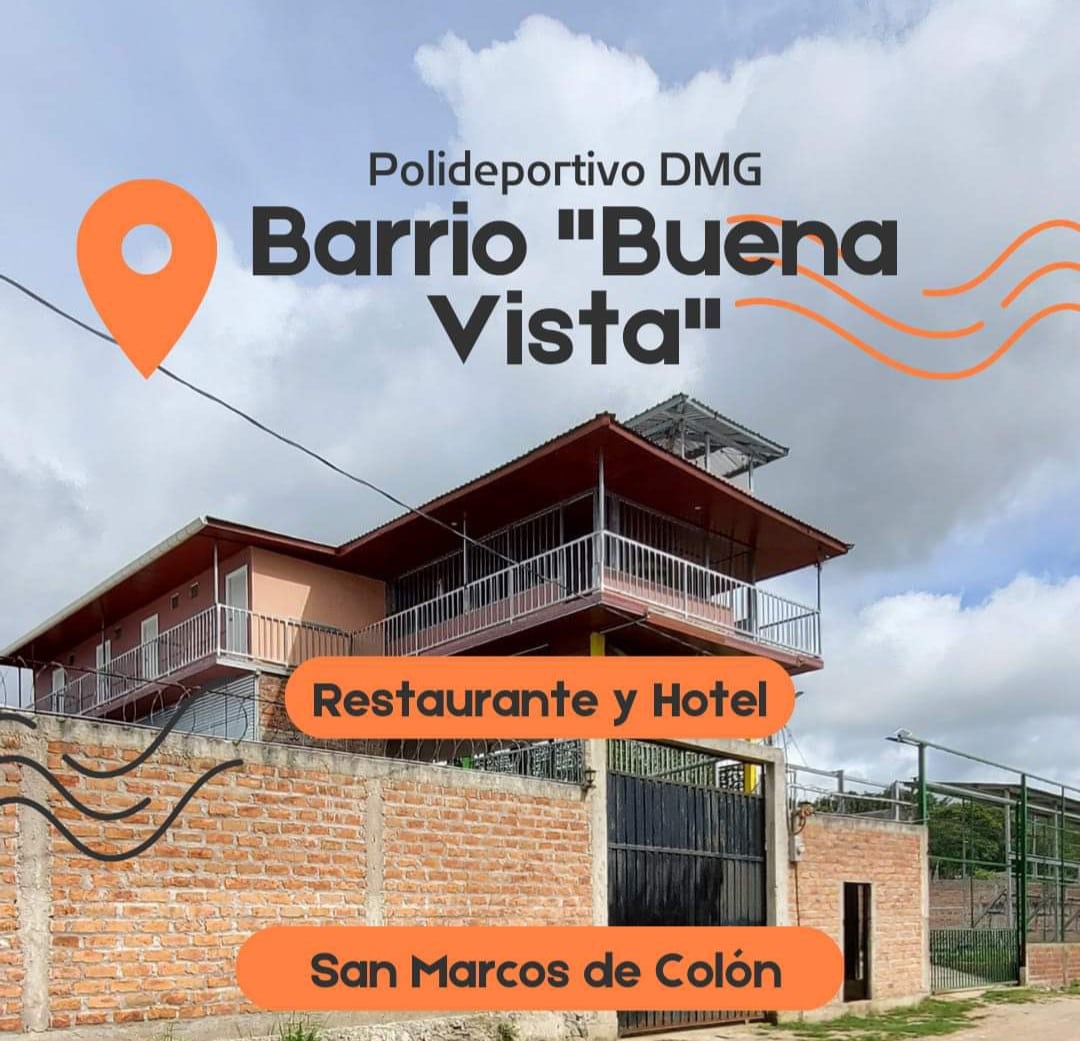 A modern two-story building is displayed, featuring a wrap-around balcony on the upper level. The exterior combines brick and contrasting colors, with a clear sign indicating a restaurant and hotel. Fencing surrounds the property, contributing to a private and secure environment.