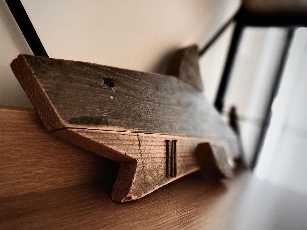 A handcrafted wooden shark sculpture rests on a smooth wooden shelf. The natural texture of the wood is highlighted, showcasing its grain and unique markings. The sculpture's streamlined shape suggests movement, adding a touch of artistic charm to the minimalist decor.