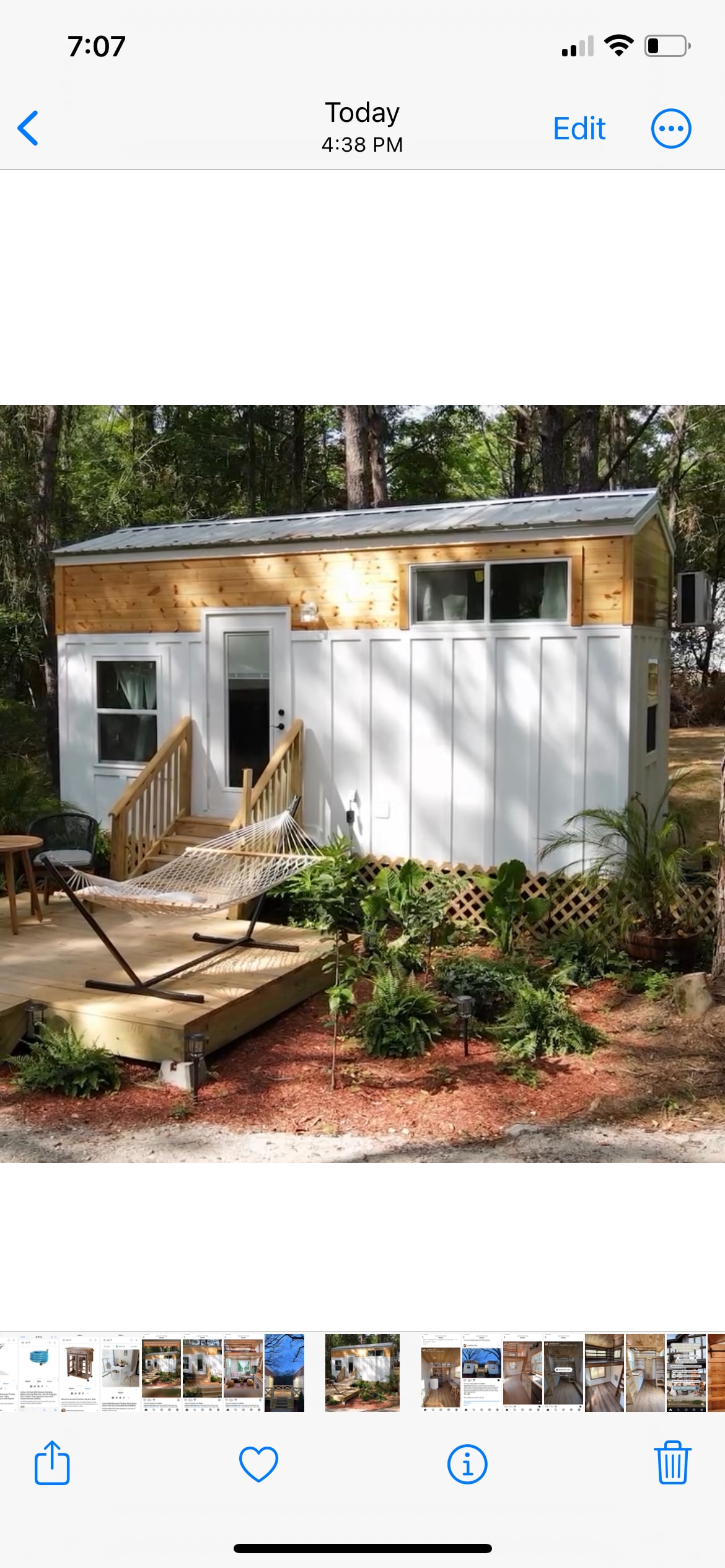 A modern tiny house is showcased with wooden accents and a light-colored exterior. A small deck leads to the entrance, featuring steps and a railing. Nearby, a hammock is suspended between two posts, surrounded by lush greenery and colorful landscaping.