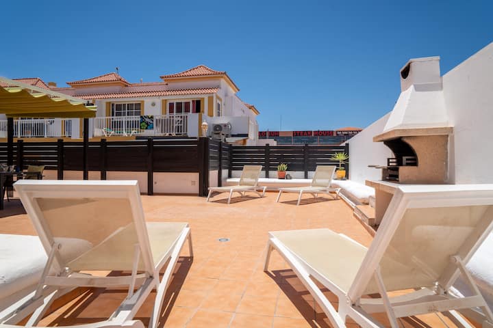 Terraza con tumbonas y barbacoa, con vistas a los tejados de la urbanización.