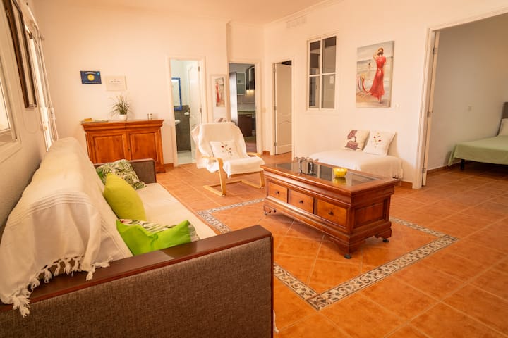Zona de estar con sofás vestidos en blanco, mesa de madera y mucha luz natural.