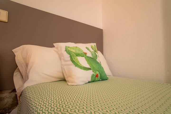 Detalle de la cama del dormitorio 2 con cojín canario: un guiño isleño lleno de color.