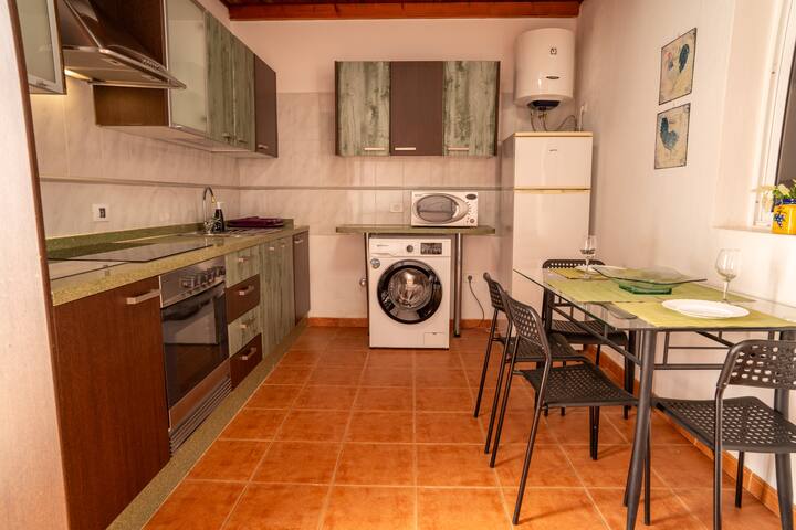 Cocina completa con lavadora, horno y mesa para comer: práctica y bien equipada.