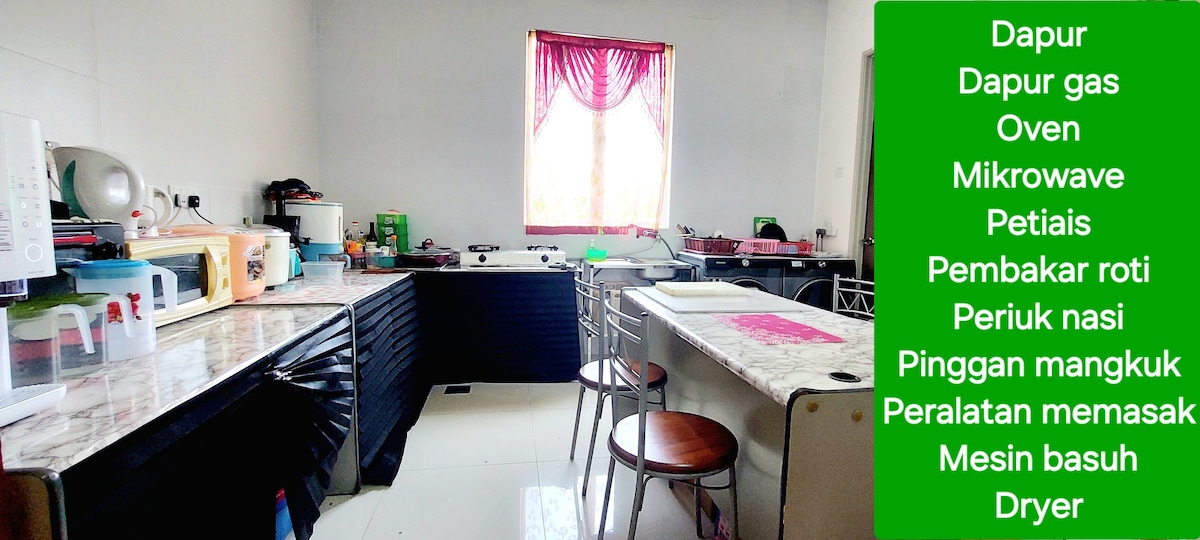 A functional kitchen is presented, featuring a gas stove, microwave, and oven. Countertops are equipped with cooking utensils and a rice cooker. Bar stools are positioned around an island, while a window with sheer curtains allows natural light to enter the space.