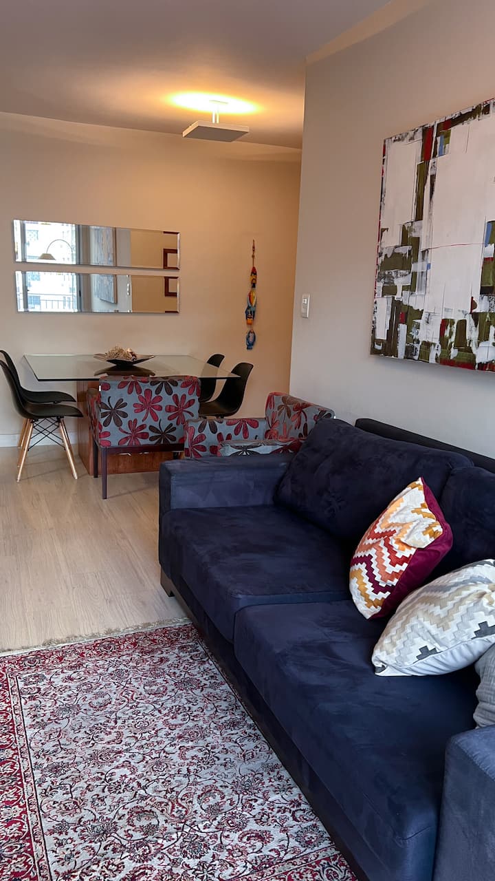 Pohovka, ktorá môže byť použitá ako posteľ, odstránenie veľkých vankúšov, koberca a v pozadí jedálenský stôl 