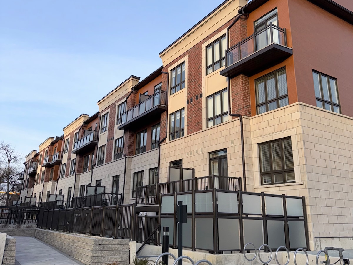 The exterior of a modern multi-unit building is displayed, featuring a blend of brick and stone materials. Large windows are observed, providing ample natural light, while several balconies are visible, enhancing the architectural design. A well-maintained pathway leads to the entrance.