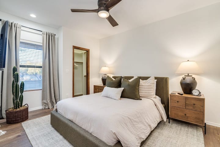 This inviting guest room features a comfortable queen bed styled with serene earth tones. Complete with a cooling ceiling fan, bedside charging space, and a convenient walk-in closet.