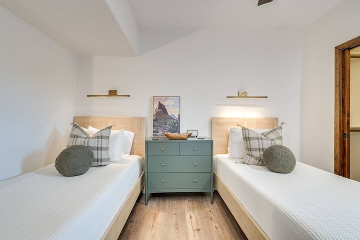 This charming guest bedroom features two comfortable single beds with stylish woven cane headboards and a central sage green dresser. A flexible sleeping arrangement tailored perfectly for kids, siblings, or friends traveling together.