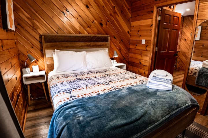 Rustige hoofdslaapkamer – Drijf in een goede nachtrust op een zacht bed omgeven door warme houten accenten en zachte verlichting. 