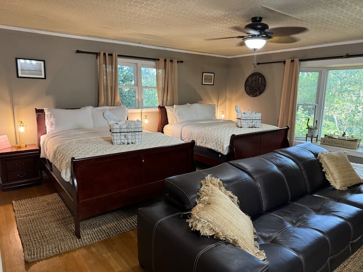 Priestranná spálňa s dvoma elegantnými drevenými manželskými posteľami s útulnou posteľnou bielizňou, mäkkou koženou pohovkou na leňošenie a veľkými oknami, ktoré zapĺňajú priestor prirodzeným svetlom a pokojným výhľadom.