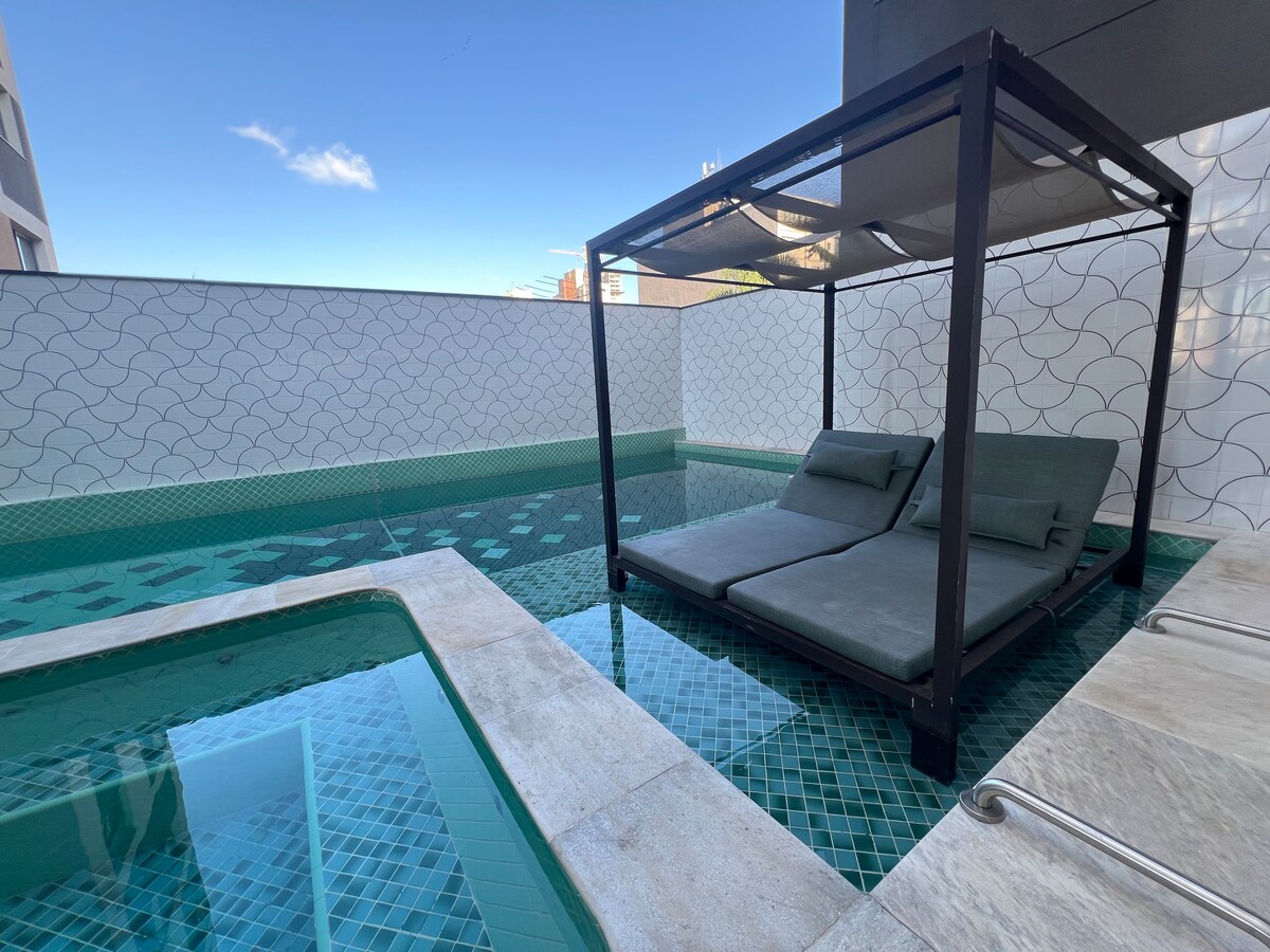 A refreshing pool area is highlighted, featuring a jacuzzi and a shaded lounge area with comfortable seating. The turquoise water reflects the clear blue sky, while textured tiles surround the pool, enhancing the inviting atmosphere.