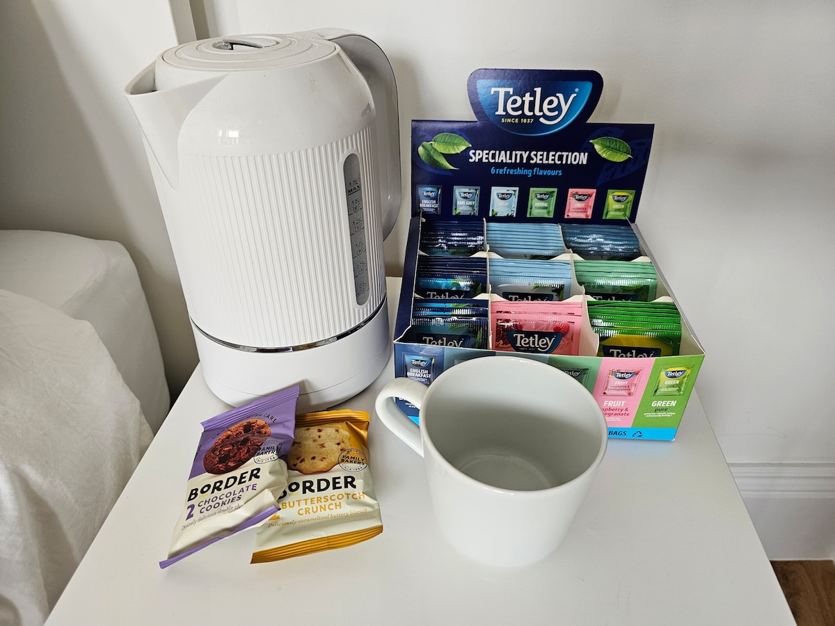 A kettle is positioned next to a selection of Tetley tea bags organized by flavor. Two packages of Border biscuits are displayed alongside a white cup, inviting guests to enjoy a relaxing beverage.