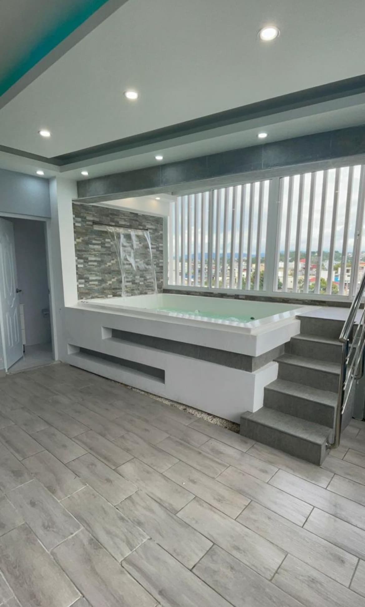 A private Jacuzzi Lounge is featured with modern design elements. A spacious jacuzzi is set against a stone accent wall, with large windows allowing natural light to fill the room. Steps lead up to the jacuzzi area, enhancing accessibility.