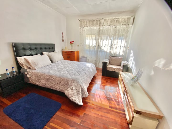 Разбудете се со утринското сонце кое струи низ големиот прозорец во оваа светла спална соба, со дрвени подови, удобен брачен кревет, простран плакар и елегантна ролетна за прилагодлива приватност