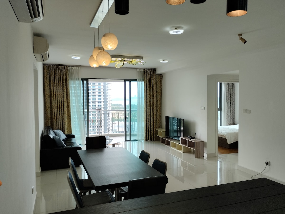 An open living and dining area is depicted, featuring a modern dining table with black chairs. A cozy seating arrangement is visible in the corner, complemented by natural light flowing through large glass doors that lead to a balcony. Nearby, a television stands on a console.