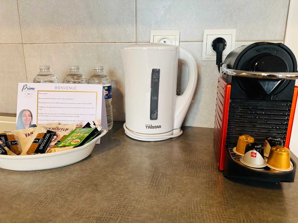 A well-appointed kitchen counter showcases a sleek electric kettle and a coffee machine. Nestled beside them are bottles of water, a welcoming note, and assorted tea and coffee options arranged on a tray, enhancing the convenience for guests.