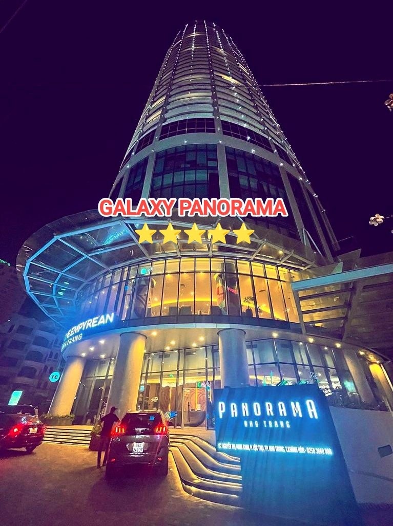 The Galaxy Panorama building is depicted at night, featuring a modern facade with multiple stories. The entrance is illuminated, highlighting the welcoming atmosphere. Vehicles are parked outside, while a prominent sign displays the name 'PANORAMA' alongside five stars.