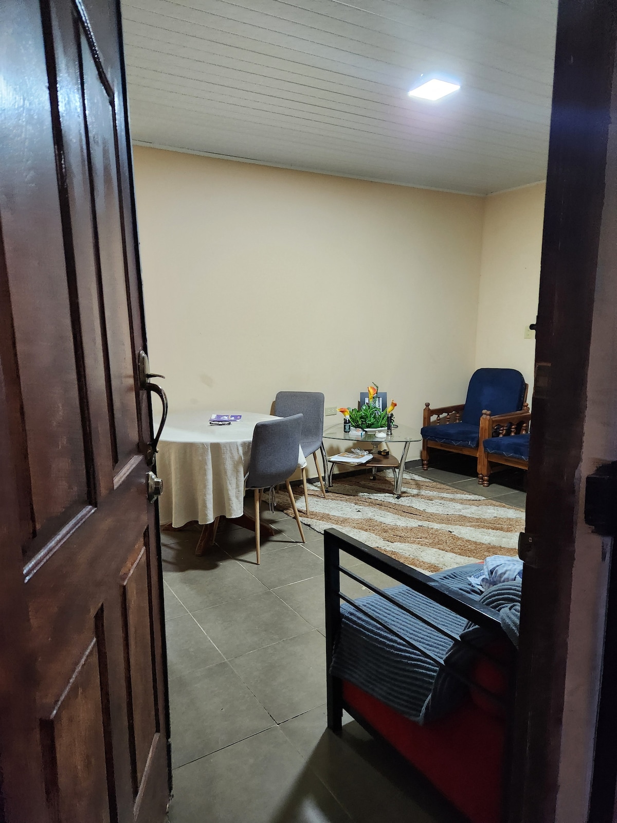 A welcoming living area is visible upon entry, featuring a circular dining table surrounded by four chairs. A small floral arrangement enhances the space, while a comfortable seating area with a wooden couch and an upholstered chair adds charm. A patterned rug lies beneath.
