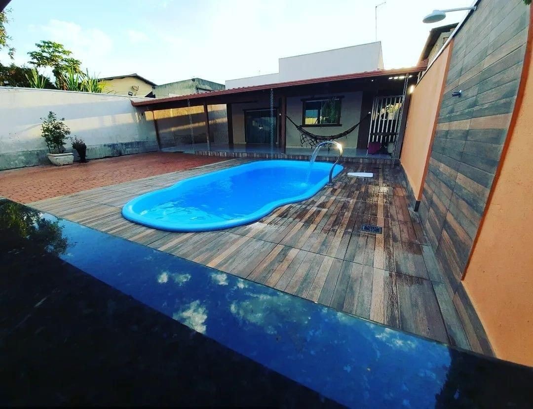 A private outdoor area features a swimming pool surrounded by wooden decking. A plant is positioned near the pool, while a patio area is visible in the background. Sunshine filters down, illuminating the pool's clear water.