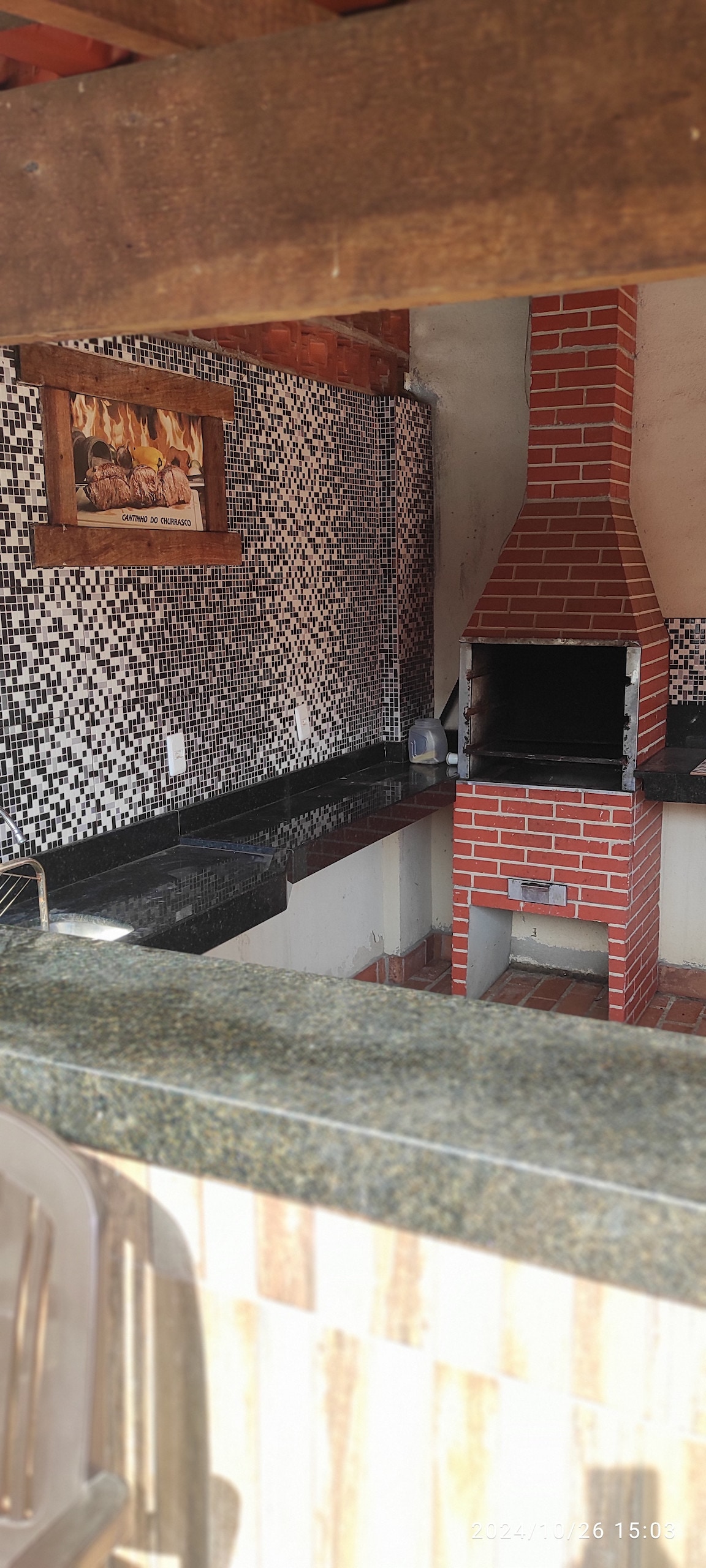 An outdoor kitchen area features a brick barbecue grill alongside a granite countertop. A mosaic-tiled wall adds texture to the space, while natural light highlights the area. The kitchen layout includes ample space for preparation and cooking.