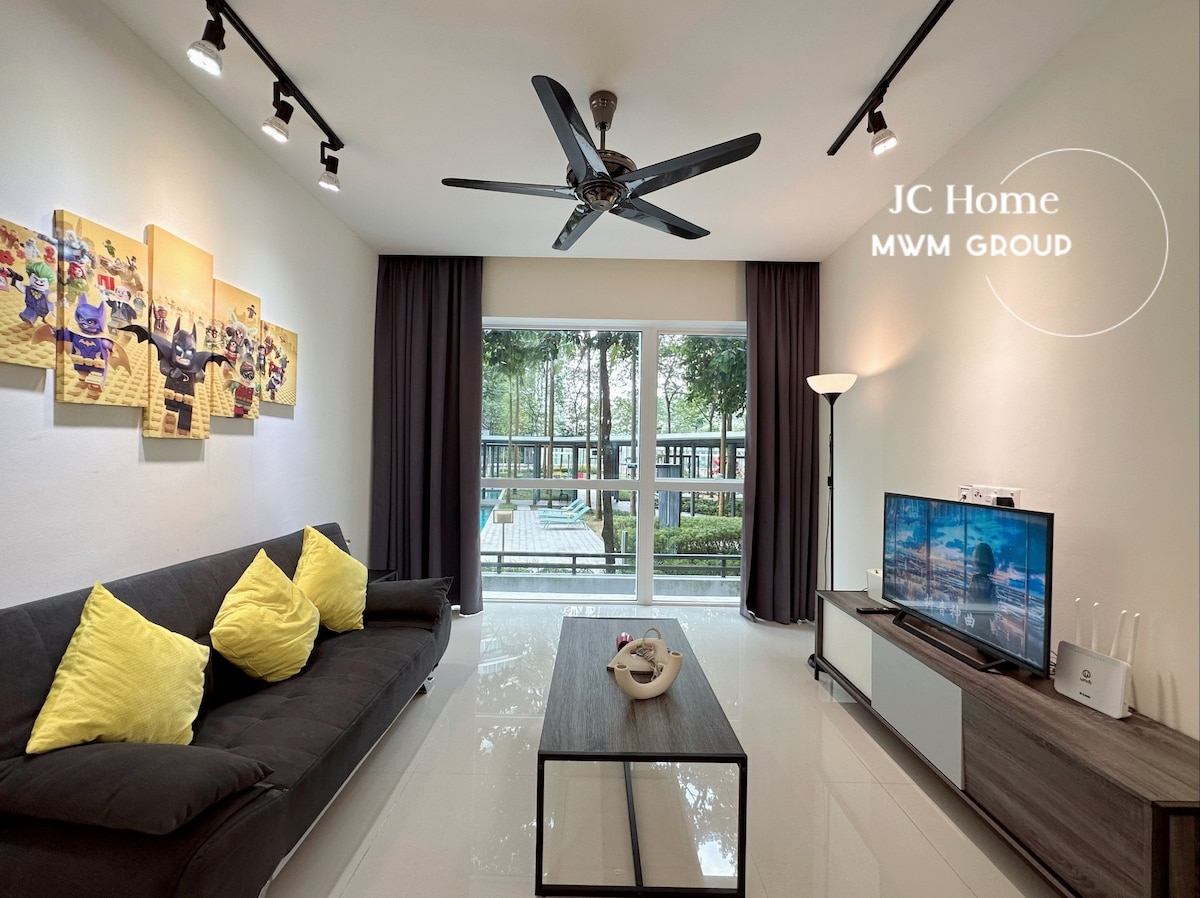 A modern living area is presented with a black sofa adorned with bright yellow cushions. A sleek coffee table sits on a glossy floor, and a flat-screen TV is positioned against white cabinetry. Natural light floods in through large windows covered by dark curtains, overlooking a green outdoor space.