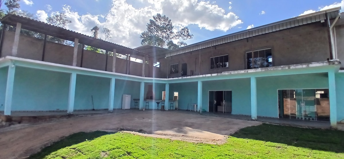A spacious outdoor area is highlighted by blue walls and lush green grass. The building features a two-story design with large glass doors and large windows that allow natural light to fill the space. A shaded patio area is visible, offering a comfortable gathering spot.