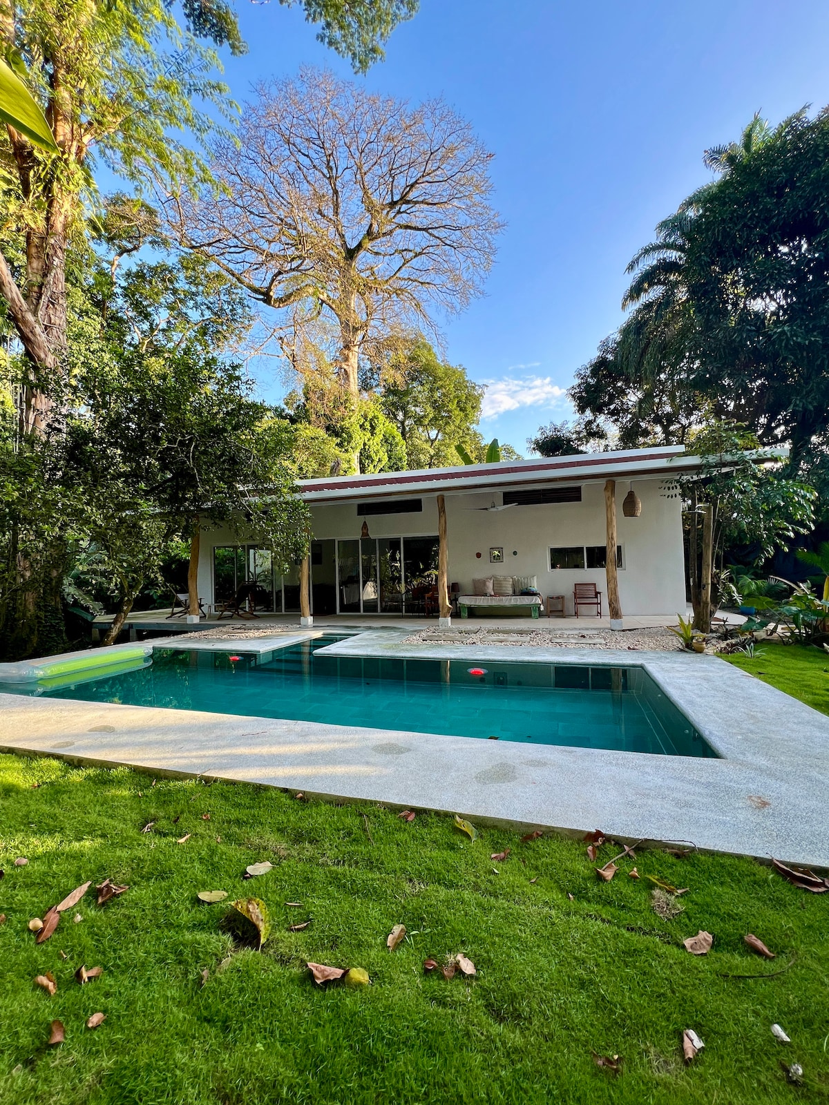The house features a spacious outdoor area with a saltwater pool, surrounded by lush greenery and tropical trees. Large glass sliding doors connect the indoor living space to the exterior, creating a seamless flow to enjoy the natural surroundings.