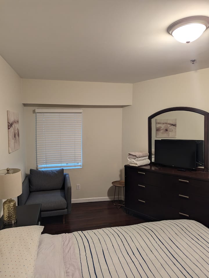 amplio dormitorio con cama tamaño Queen, tumbona y cómoda 