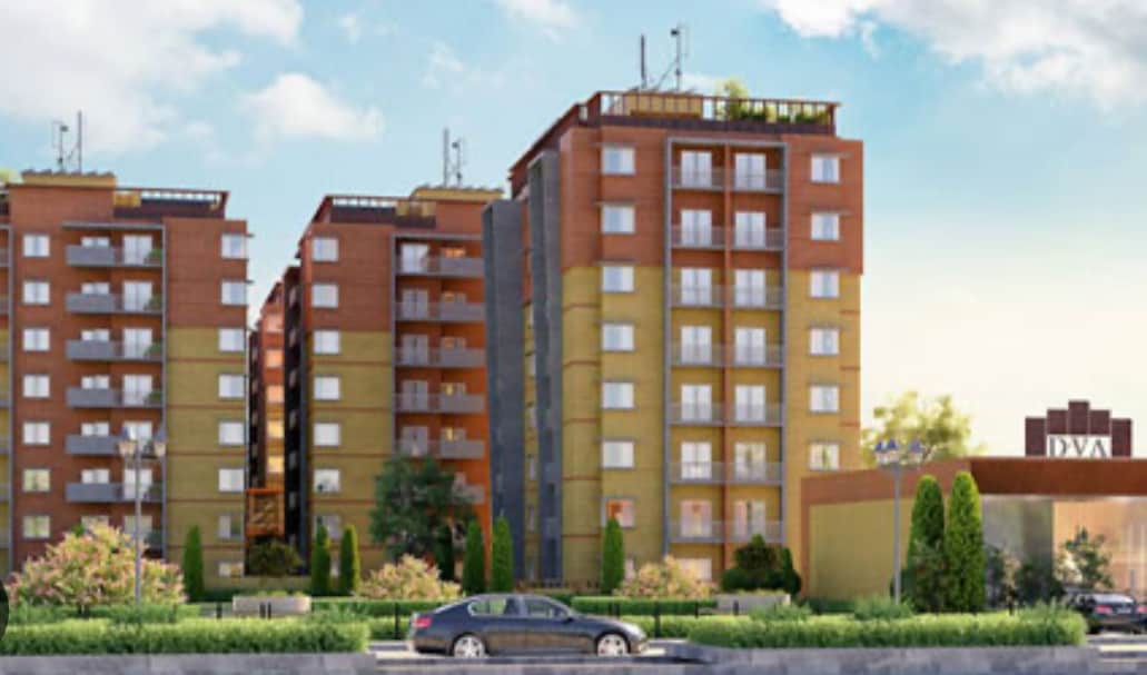 A modern apartment complex is showcased with multiple levels and a contemporary design. Green landscaping is present in the foreground, framing the building. Nearby, a well-maintained pathway leads towards the entrance, enhancing accessibility for guests.