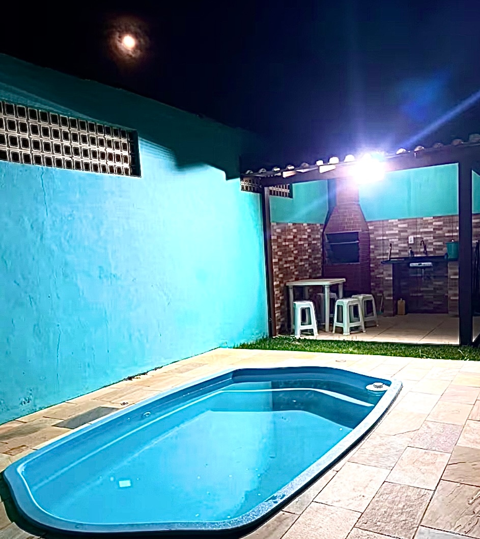 A private pool is prominently featured beside a bright turquoise wall, illuminated by ambient lighting. Adjacent to the pool, an outdoor kitchen area includes bar stools and a barbecue setup, creating a functional space for dining and relaxation.