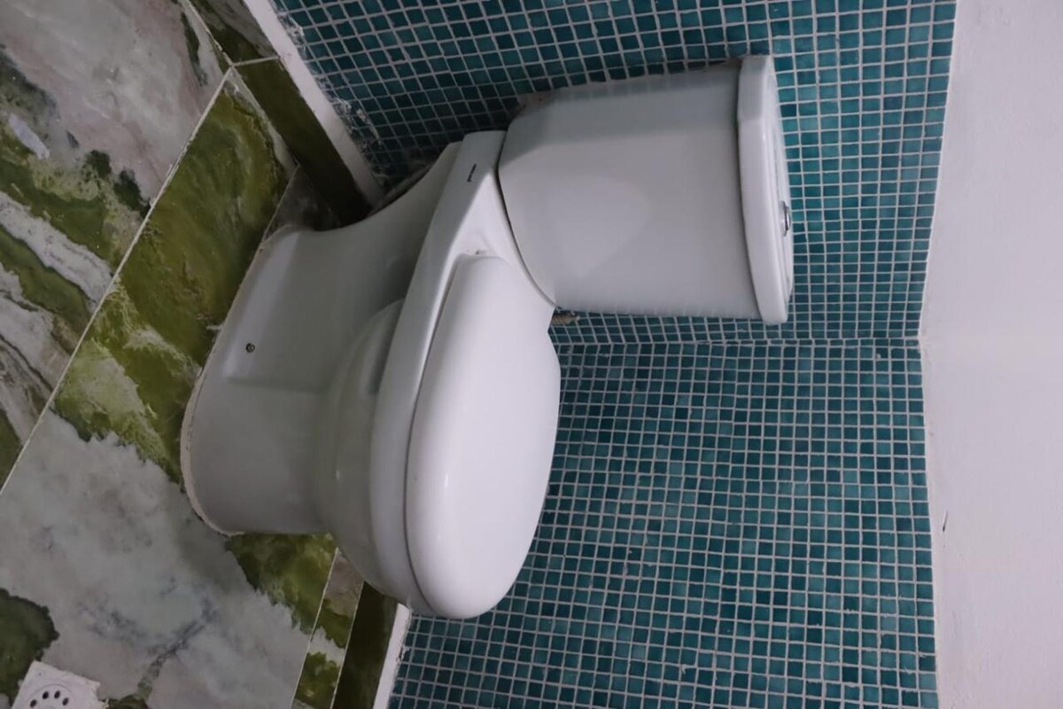 A clean white toilet is positioned against a backdrop of teal mosaic tiles. The floor features natural stone patterns, creating a simple and functional restroom space.