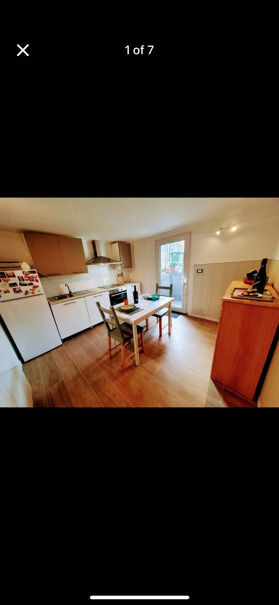 A functional kitchen area equipped with modern appliances, including a refrigerator and stove. A dining table with chairs is positioned near a window, allowing natural light to fill the space. Wooden cabinetry provides storage, complemented by a warm-toned floor.