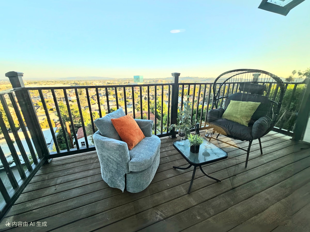A serene balcony features a stylish glass table surrounded by comfortable seating, including a gray chair and a black chair with vibrant cushions. City vistas are visible beyond the railing, allowing for a relaxing outdoor atmosphere.
