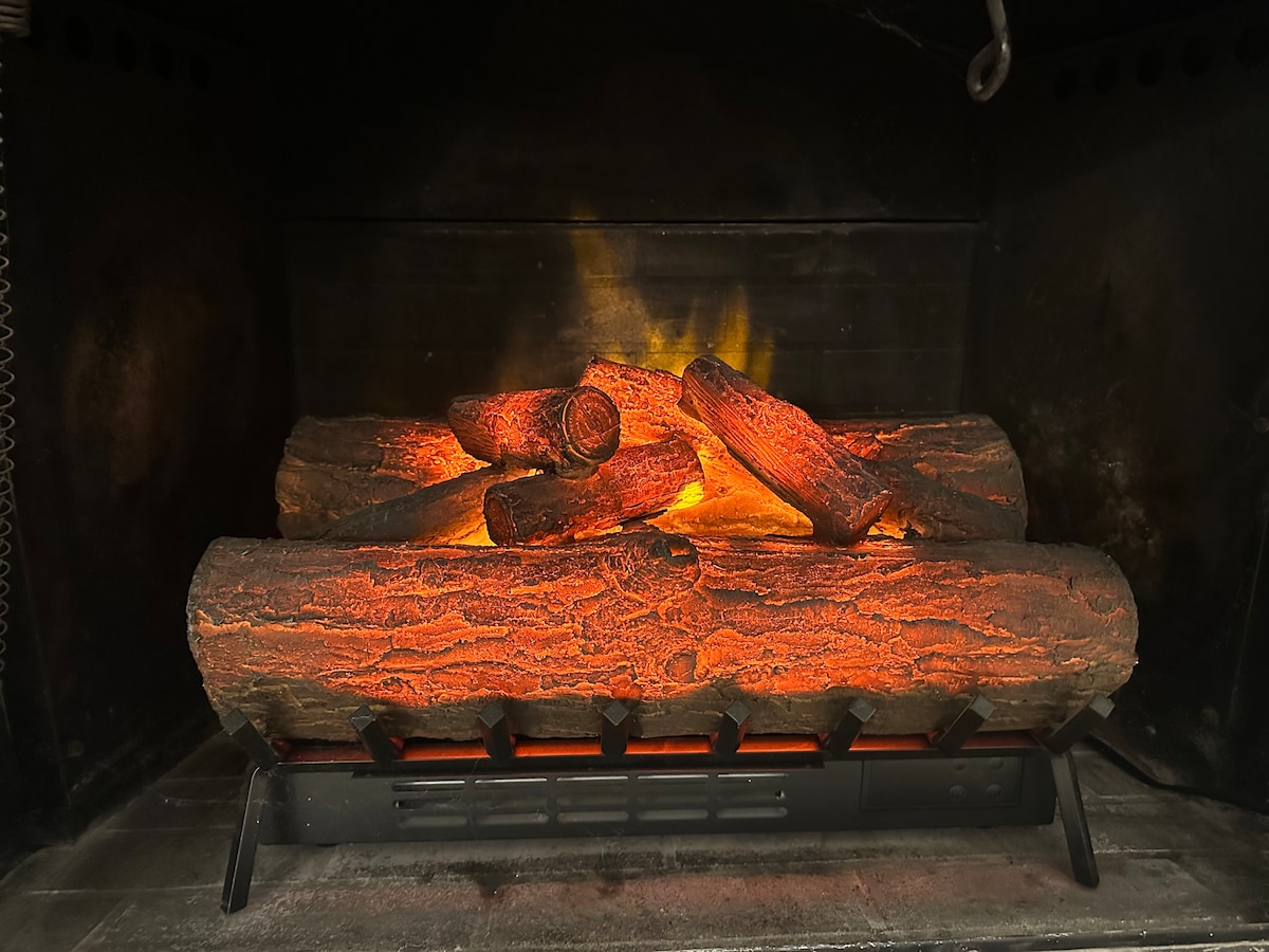 A realistic faux fireplace is showcased with glowing logs and a flickering flame effect. The design creates an inviting focal point, enhancing the cozy atmosphere of the living area.
